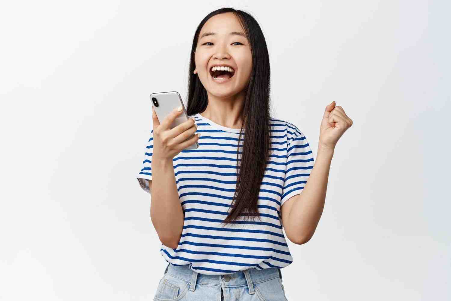 excited-asian-woman-rejoicing-from-smartphone-app-notification-winning-mobile-phone-standing-white (1)